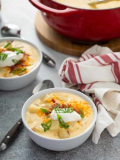 Two bowls of loaded baked potato soup on a counter in front of a dutch oven filled with soup