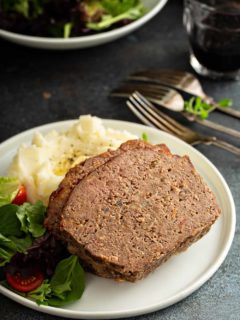 Close up of sliced meatloaf on a plate with potatoes and salad