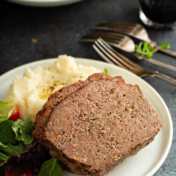 Close up of sliced meatloaf on a plate with potatoes and salad