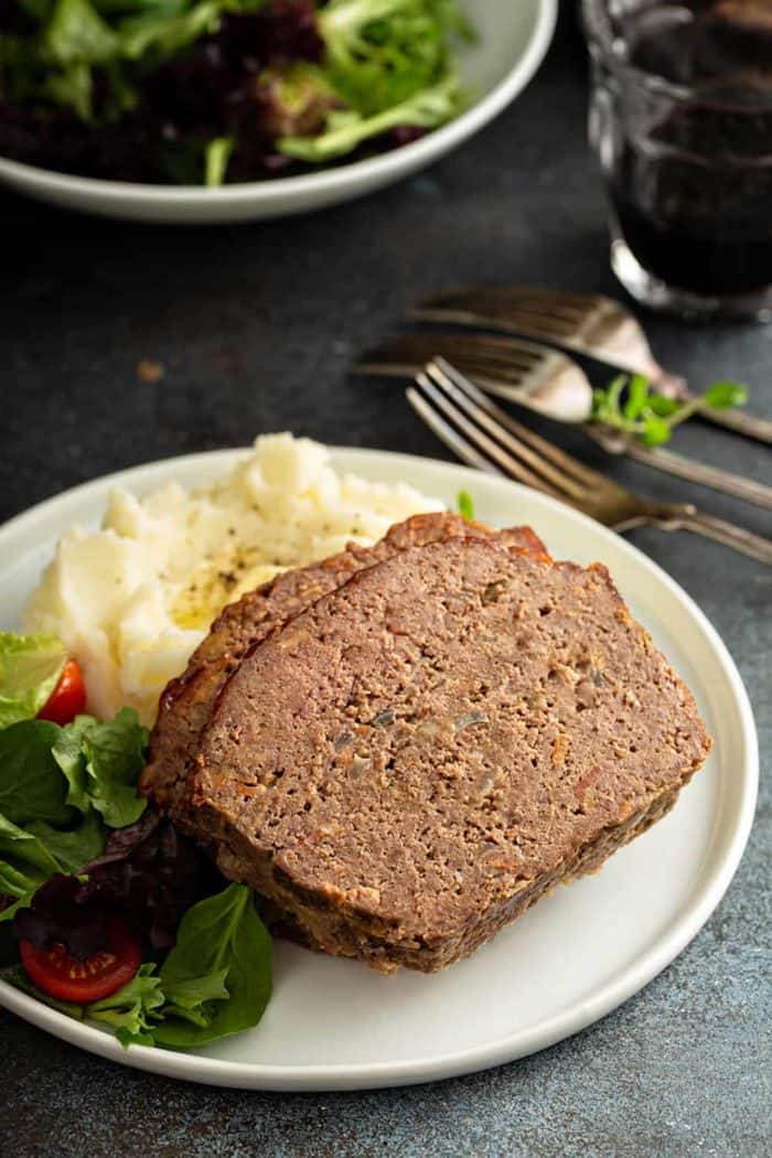 Close up of sliced meatloaf on a plate with potatoes and salad