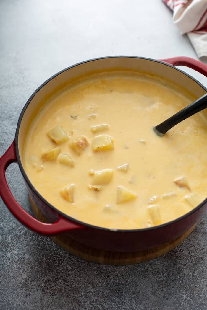 Ladle stirring cheesy potato soup in a large dutch oven