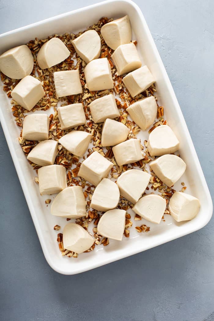 Frozen bread dough pieces on top of chopped pecans in a white baking dish