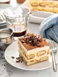 Tiramisu on a white plate, topped with chocolate curls