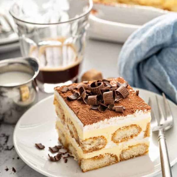 Tiramisu on a white plate, topped with chocolate curls