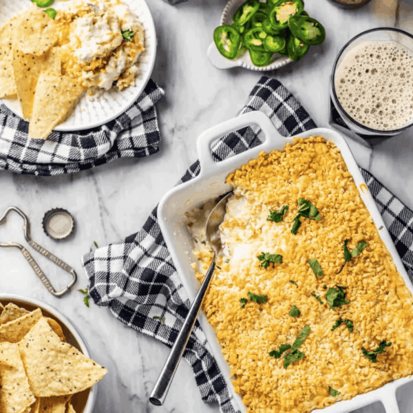 Baking dish of jalapeno popper dip on a counter surrounded by chips and beer