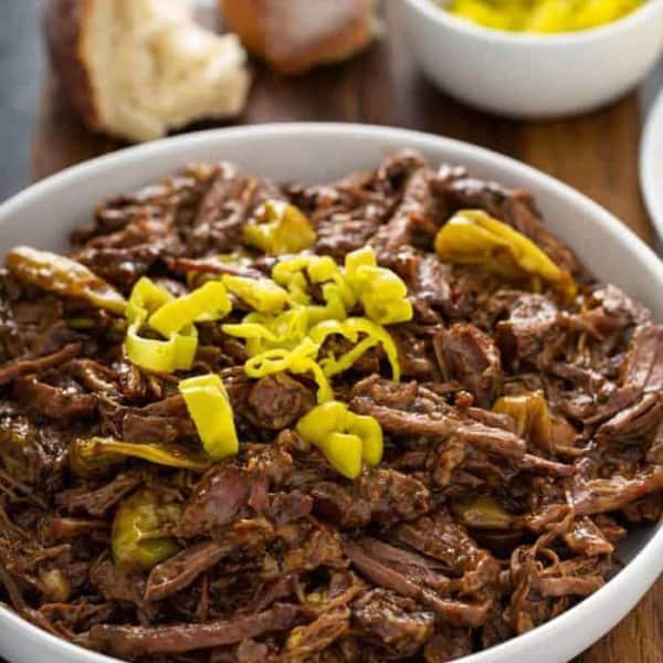 Mississippi pot roast in a white serving bowl, topped with sliced pepperoncinis