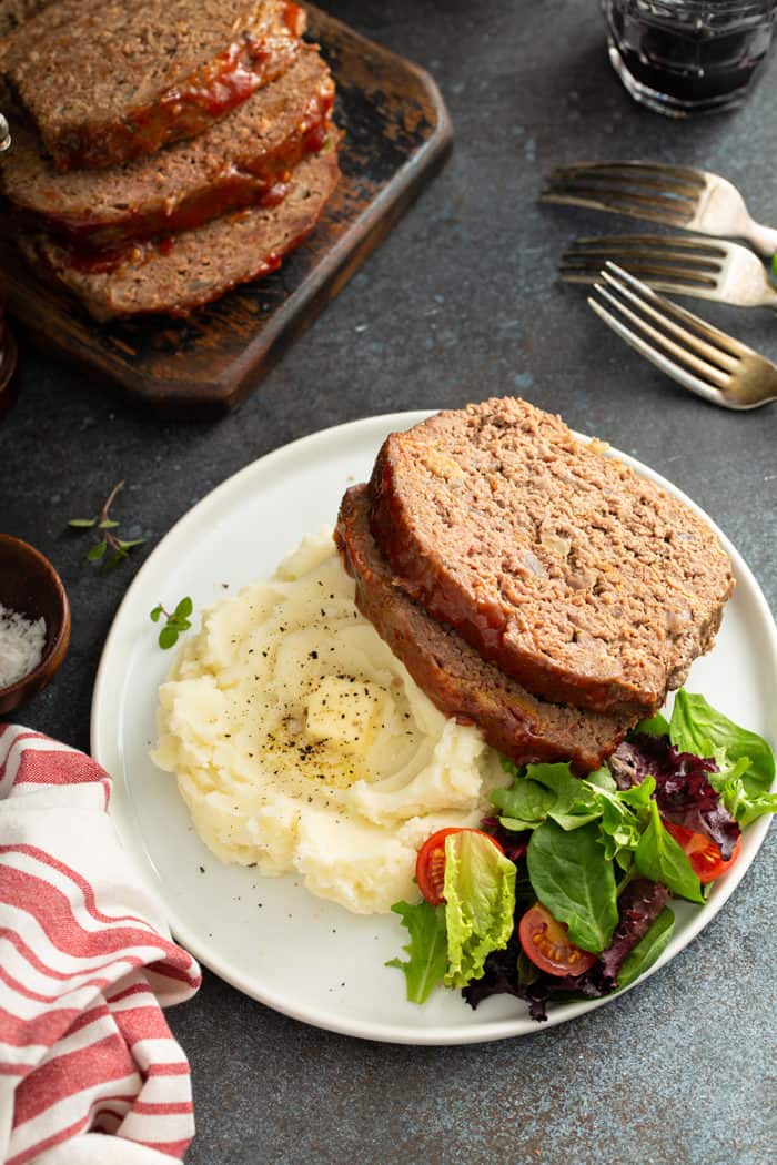 Overhead view of two slices of easy meatloaf on a plate with mashed potatoes and salad