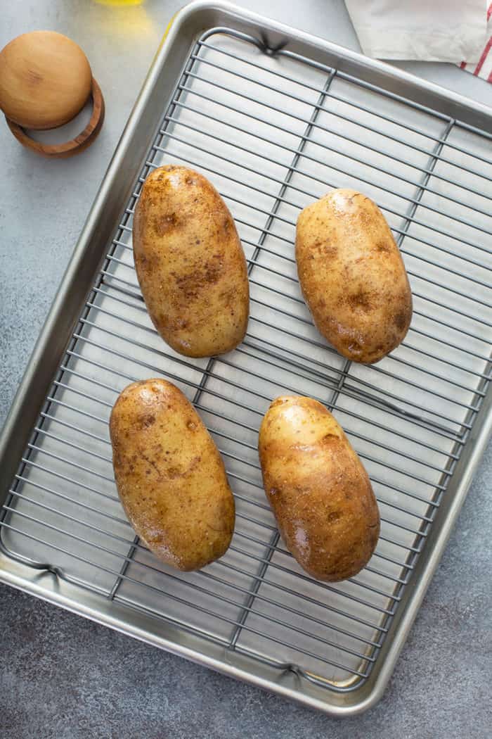 Four prepped russet potatoes on a wire rack, ready to be baked