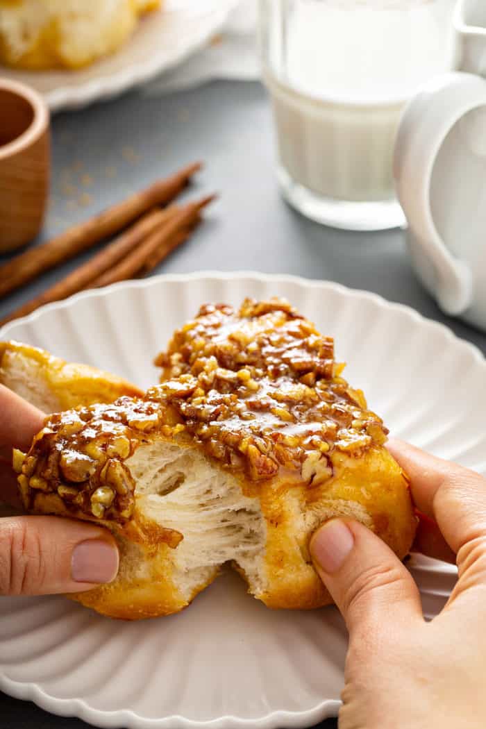 Hand pulling apart pecan sticky buns on a white plate