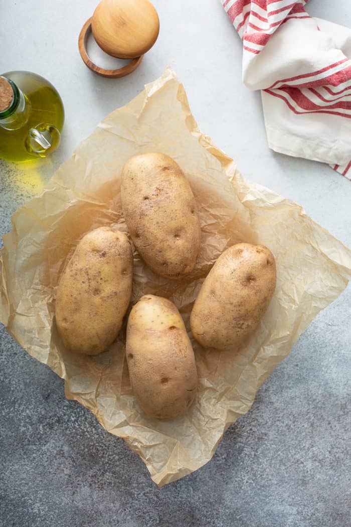 Four russet potatoes on a piece of parchment paper, ready to be prepped for baking