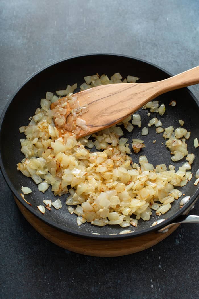 Wooden spoon stirring sauteed onions and garlic in a skillet