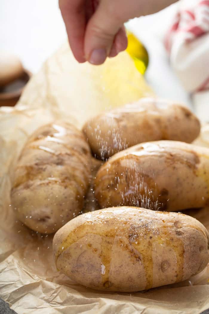 Hand sprinkling salt over four russet potatoes