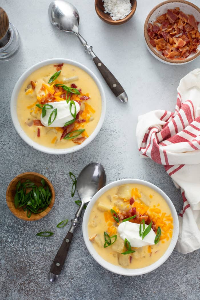Overhead view of two bowls of potato soup topped with sour cream, cheese, bacon and green onions