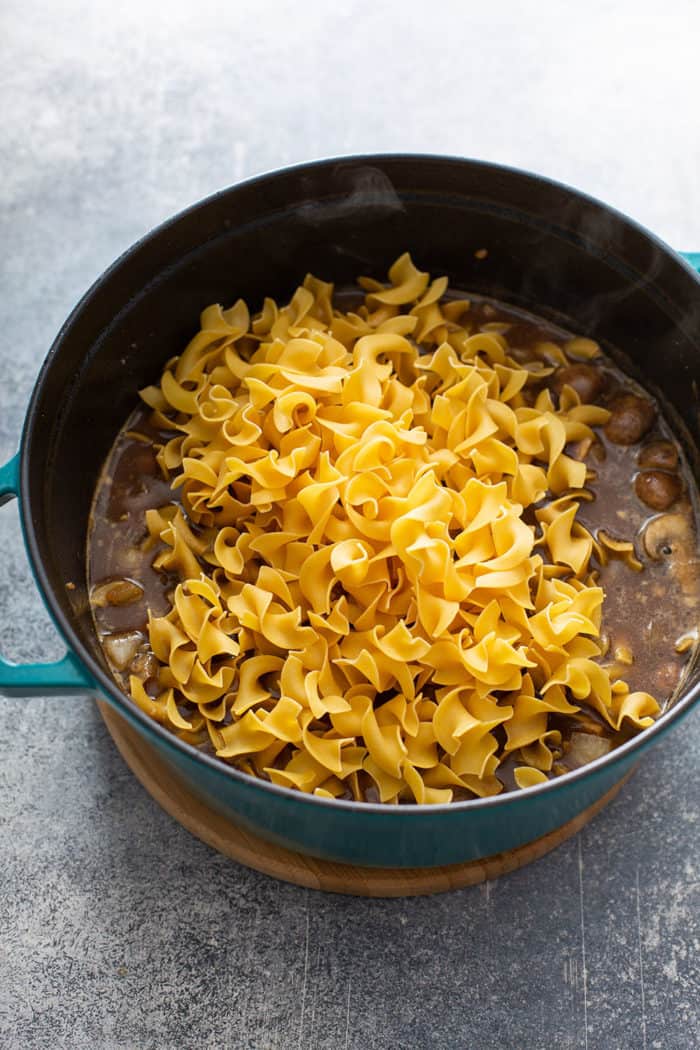 Egg noodles being added to one-pot beef stroganoff in a dutch oven