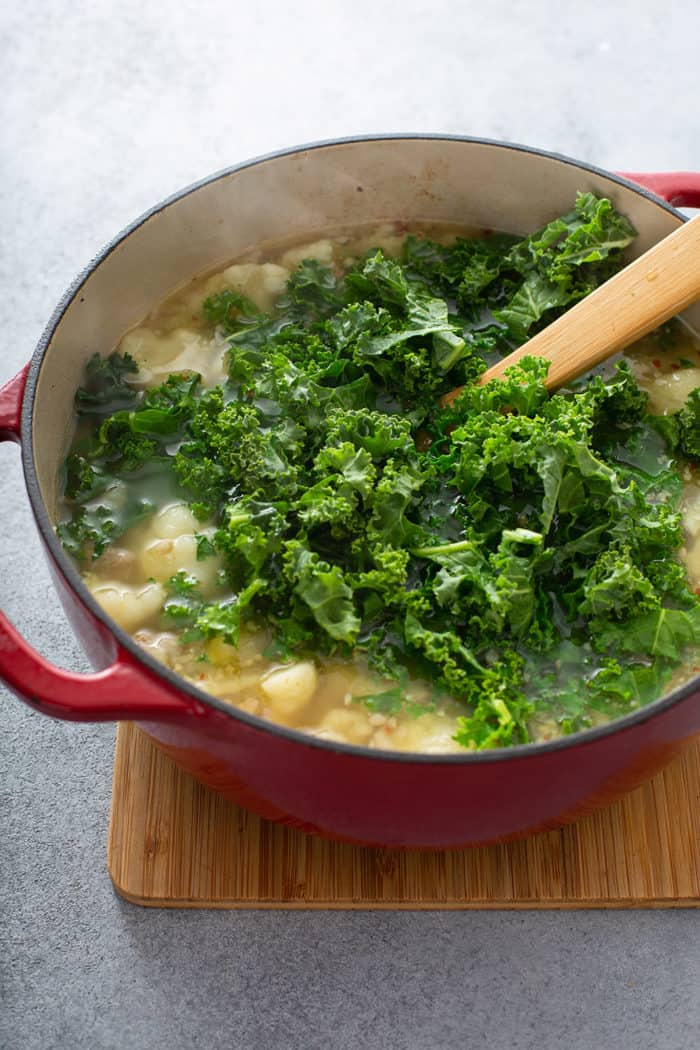 Kale being stirred into a pot of low carb zuppa toscana