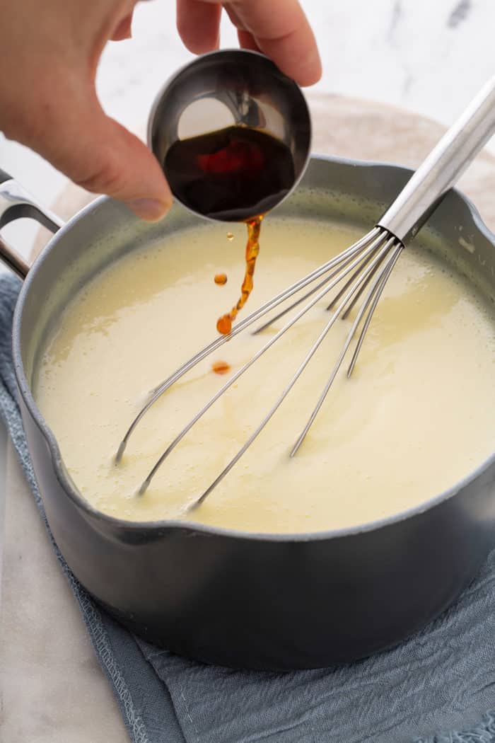 Hand pouring vanilla extract into vanilla pudding in a saucepan