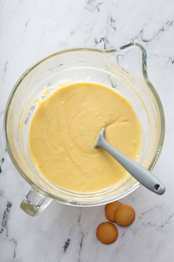 Banana cake batter in a glass mixing bowl, being stirring by a spatula