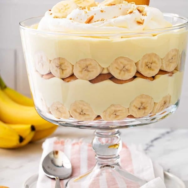 Layered banana pudding in a trifle dish, topped with whipped cream and sliced bananas