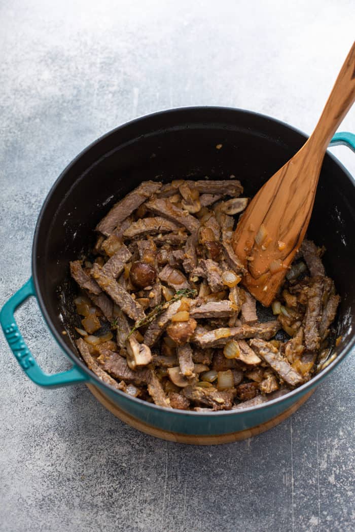 Spoon stirring together sauteed mushrooms, onions, steak, and thyme for beef stroganoff