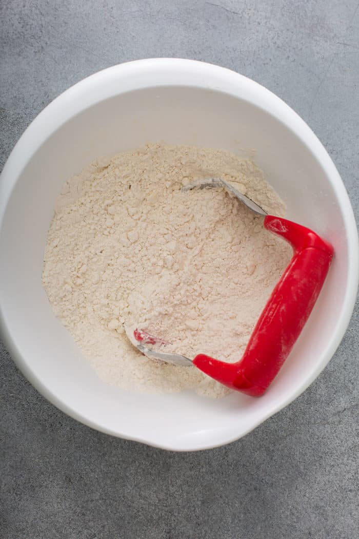 Dough blade in a white mixing bowl with a mixture of butter and flour cut together