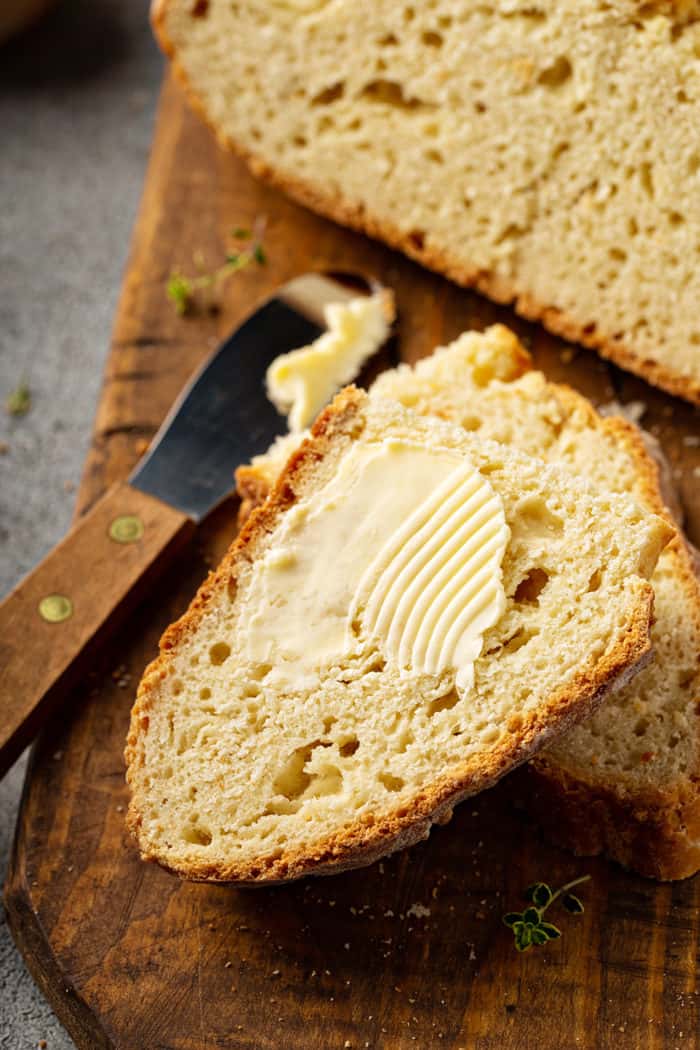 Slice of Irish soda bread topped with butter on a wooden board, next to a butter knife