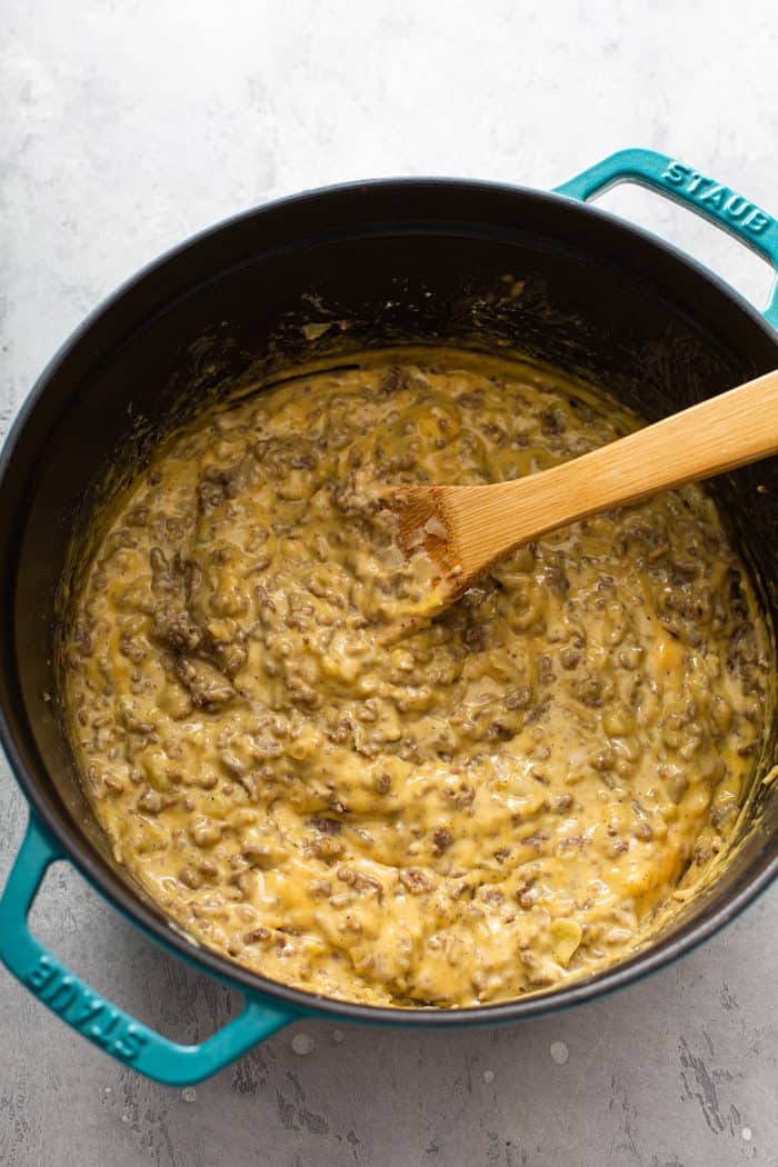 Wooden spoon stirring cheeseburger soup base in a dutch oven