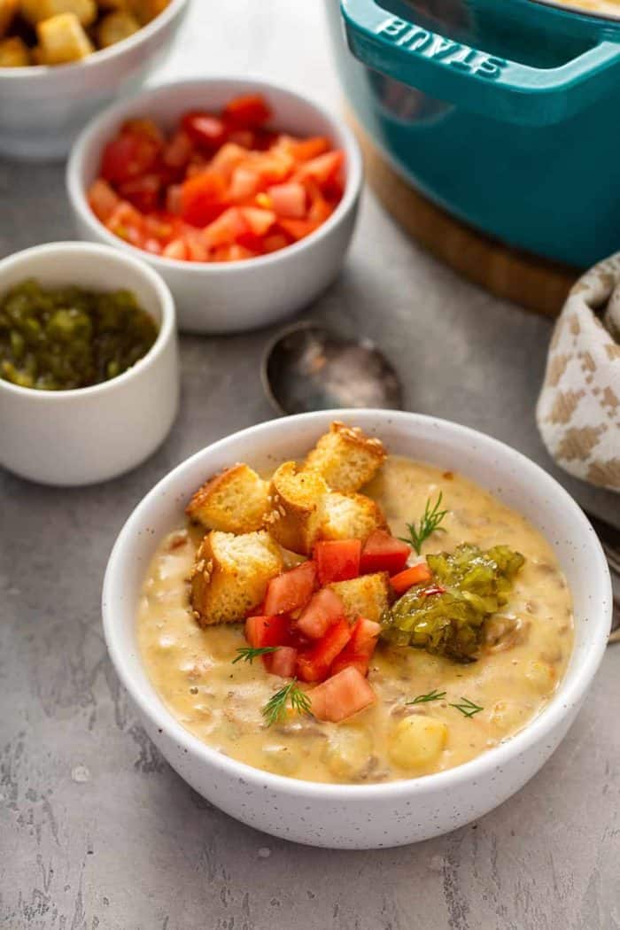 Bowl of cheeseburger soup topped with croutons, diced tomatoes and pickle relish