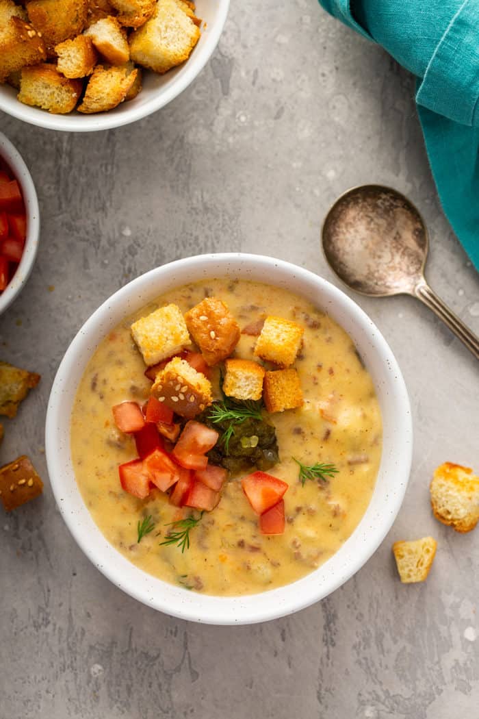 Overhead view of cheeseburger soup topped with croutons and pickles in a white bowl