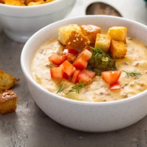 White bowl filled with cheeseburger soup topped with relish, tomatoes and croutons