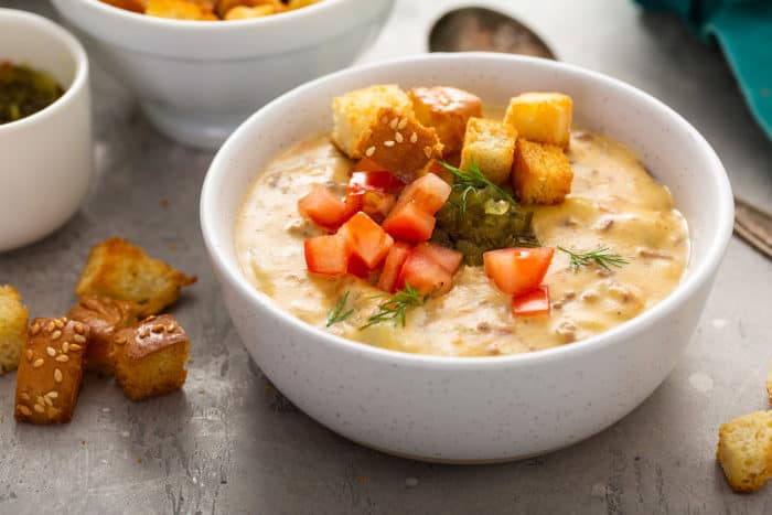 White bowl filled with cheeseburger soup topped with relish, tomatoes and croutons