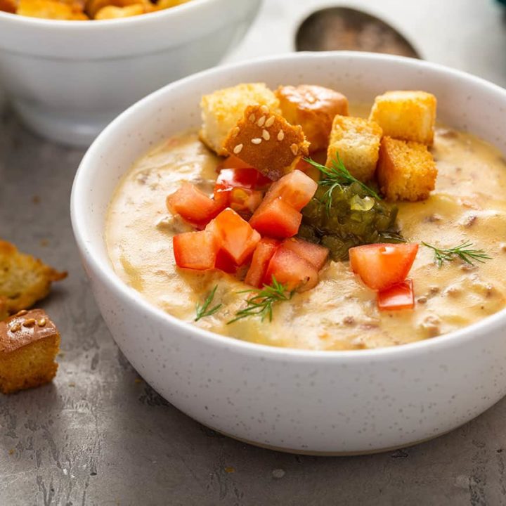 White bowl filled with cheeseburger soup topped with relish, tomatoes and croutons