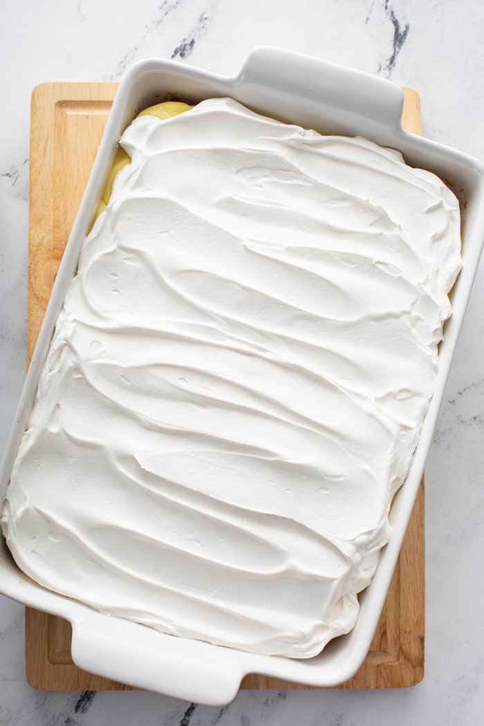 Whipped topping on top of banana pudding cake in a white baking dish