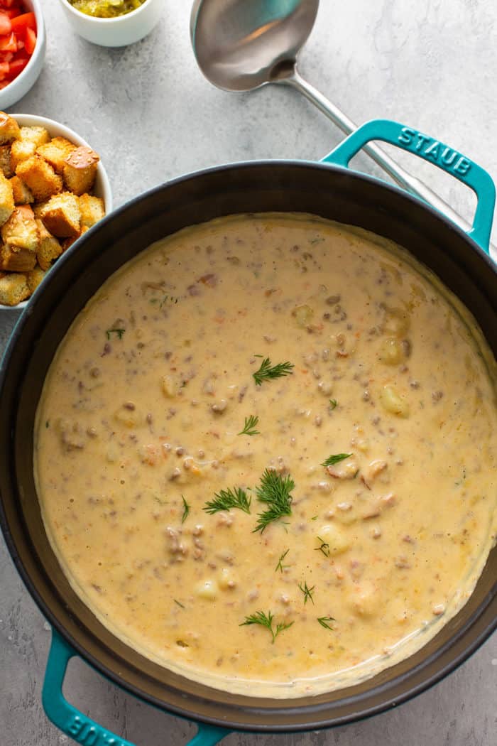 Overhead view of cheeseburger soup in a cast iron dutch oven next to a bowl of hamburger bun croutons