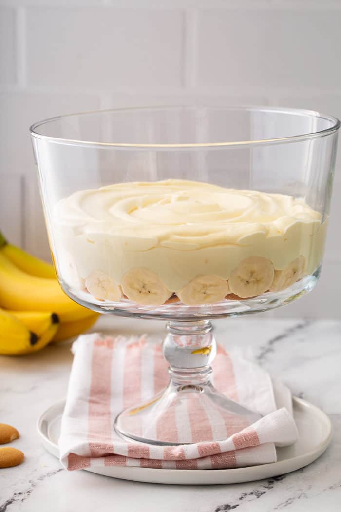 One layer of banana pudding in a trifle dish with bananas in the background