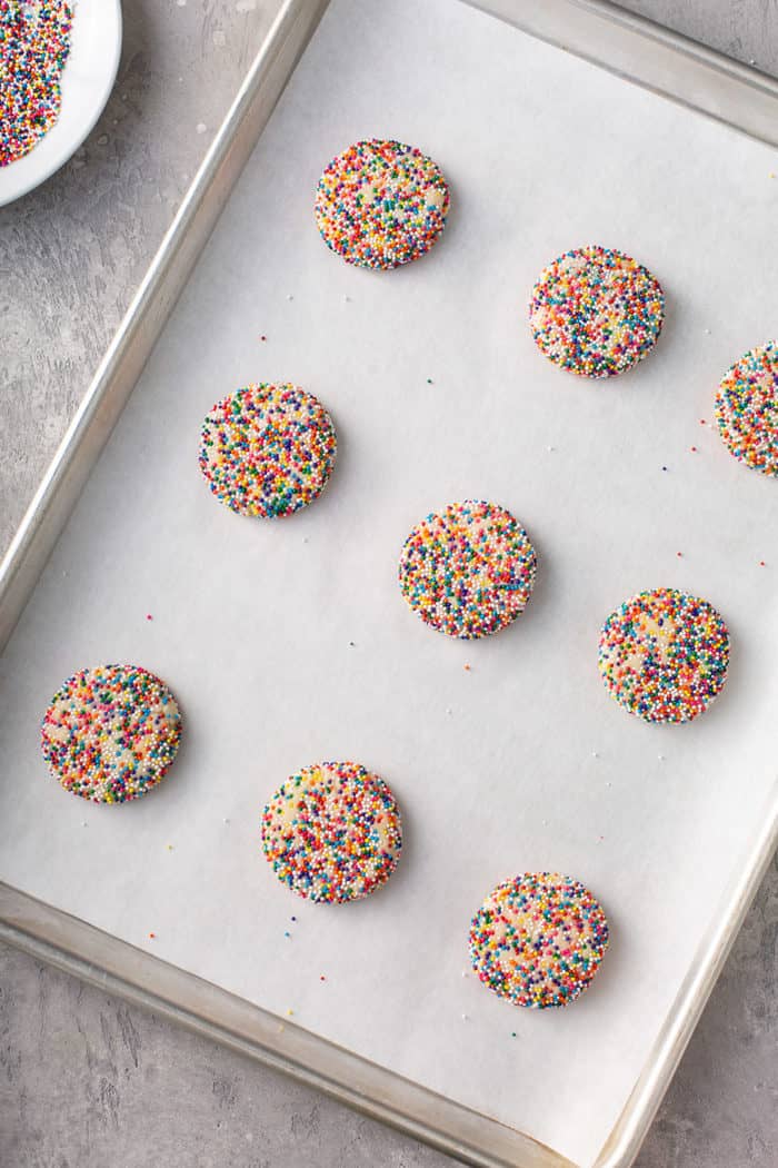 Flattened balls of funfetti cookie dough on a parchment-lined baking sheet