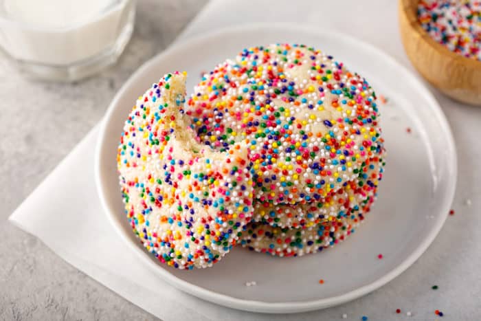 Funfetti cookie with a bite taken out of it leaning against a stack of 3 cookies on a plate