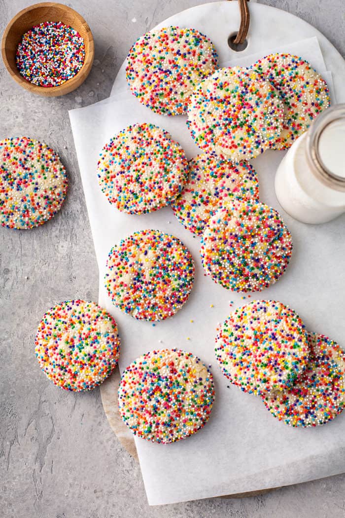 Funfetti cookies scattered across a piece of parchment paper, next to a glass of milk