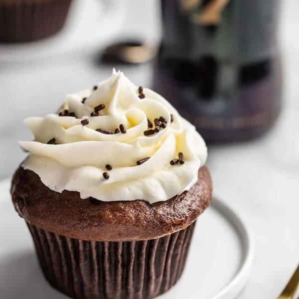 Guinness chocolate cupcake topped with vanilla buttercream and chocolate jimmies on a white plate in front of a Guinness bottle