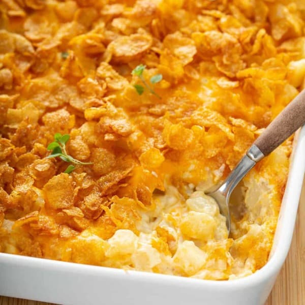 Spoon digging into the corner of a hash brown casserole in a white baking dish