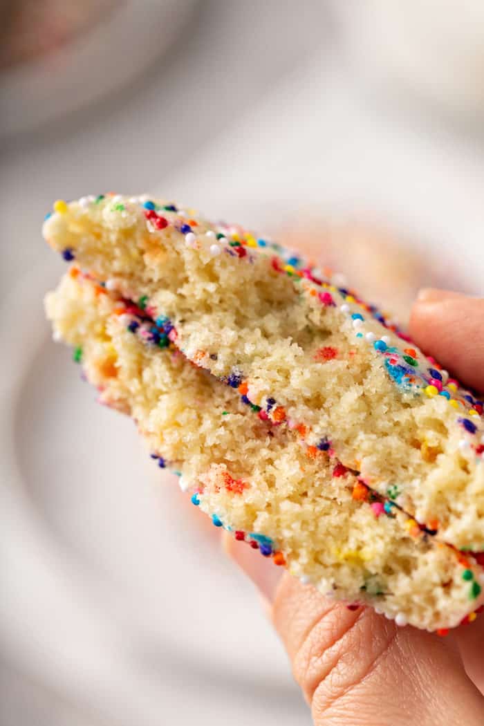 Hand holding up two halves of a funfetti cookie to show the inside of the cookie
