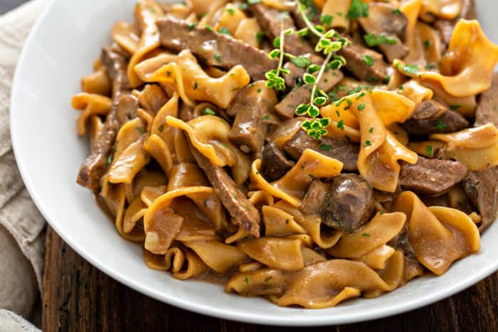 Close up of one-pot beef stroganoff in a white serving bowl, garnished with fresh thyme