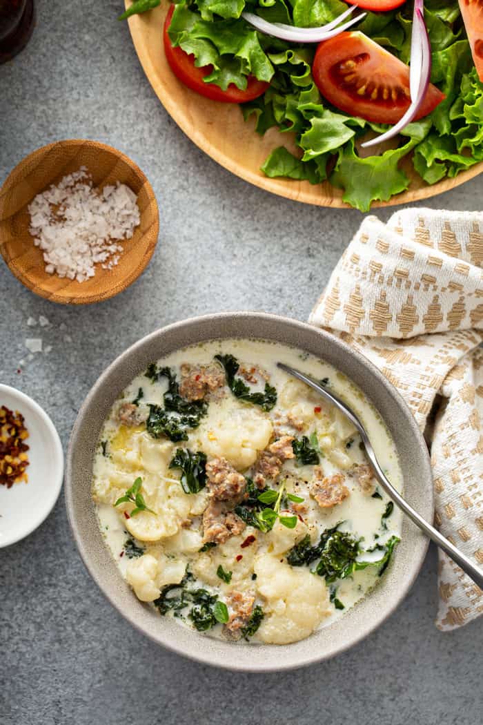 Overhead view of a bowl of zuppa toscana alongside a green salad and a cloth napkin