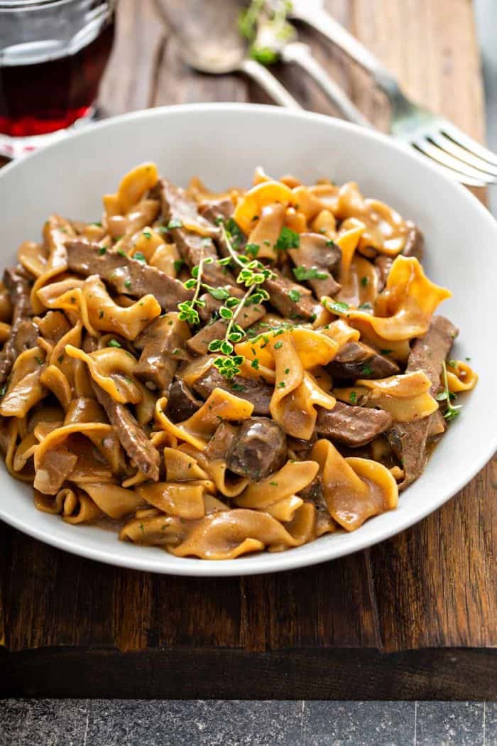 Bowl of one-pot beef stroganoff, topped with fresh thyme, on a wooden board
