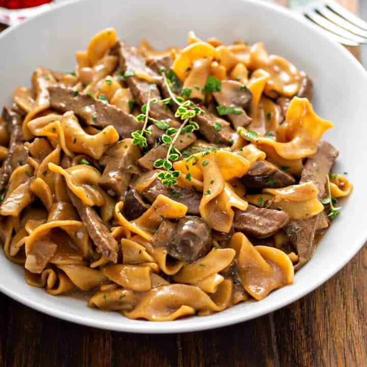 Bowl of one-pot beef stroganoff, topped with fresh thyme, on a wooden board