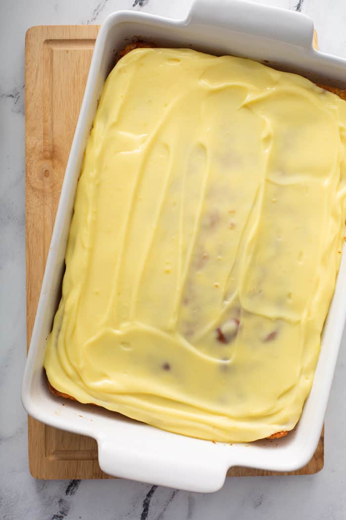Pudding spread over the top of banana cake in a white baking dish