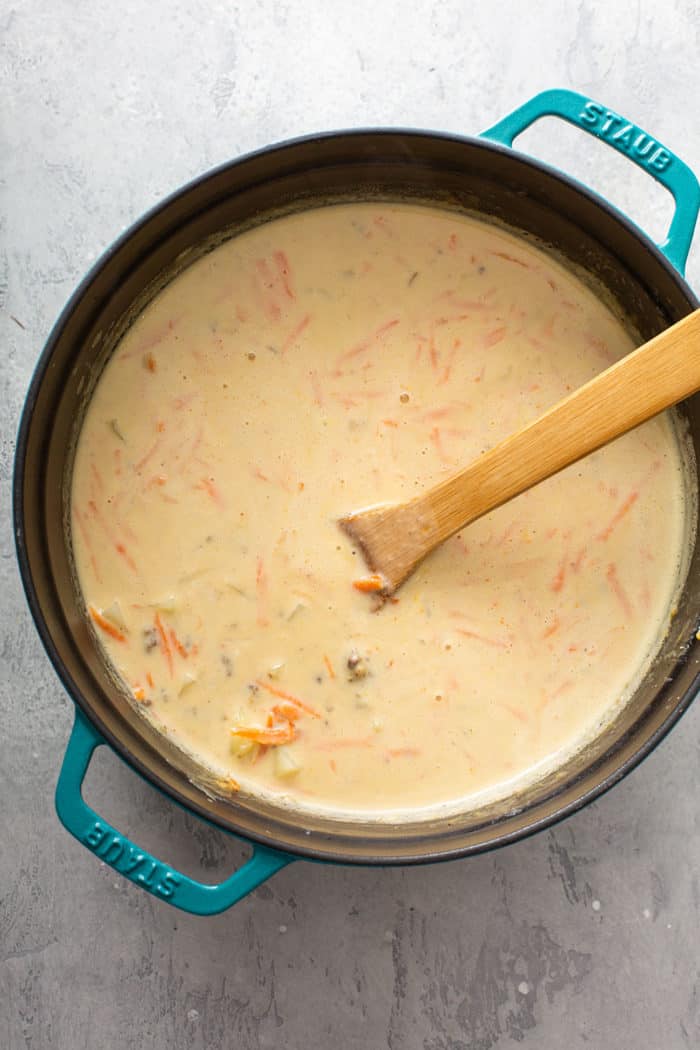 Wooden spoon stirring cheeseburger soup before it has thickened