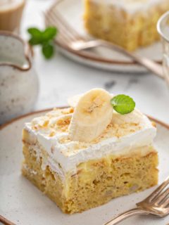 Slice of banana pudding poke cake garnished with a slice of banana on a white plate