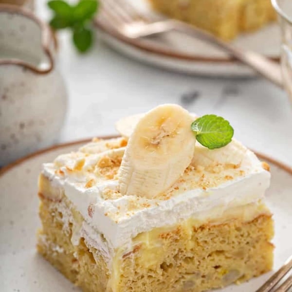 Slice of banana pudding poke cake garnished with a slice of banana on a white plate