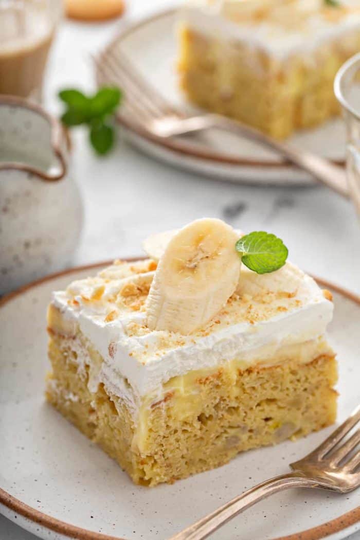 Slice of banana pudding poke cake garnished with a slice of banana on a white plate