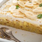 Banana pudding poke cake in a white baking dish with several slices removed to show the inside view of the cake